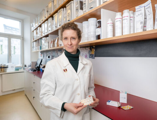 Apothekerin in weißem Kittel hält eine Blisterpackung mit Tabletten in der Hand.