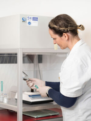 Apothekerin zieht eine Flüssigkeit mit einer Spritze in einem sterilen Laborbereich auf.