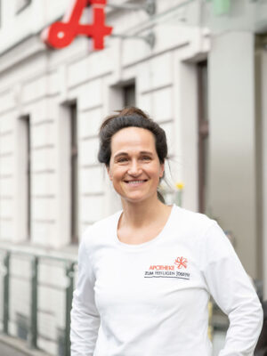 Mitarbeiterin der Apotheke Zum Heiligen Joseph lächelt vor der Apotheke.