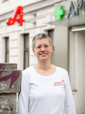 Apothekerin mit Kurzhaarschnitt und Brille vor der Apotheke.