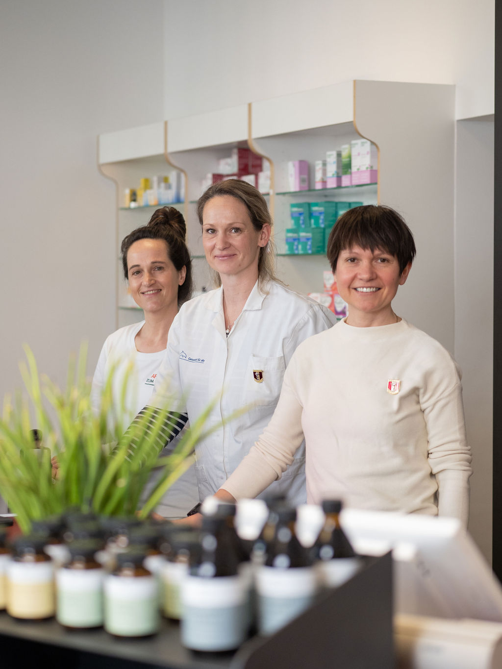 Drei Apothekerinnen stehen freundlich lächelnd hinter dem Verkaufstresen.